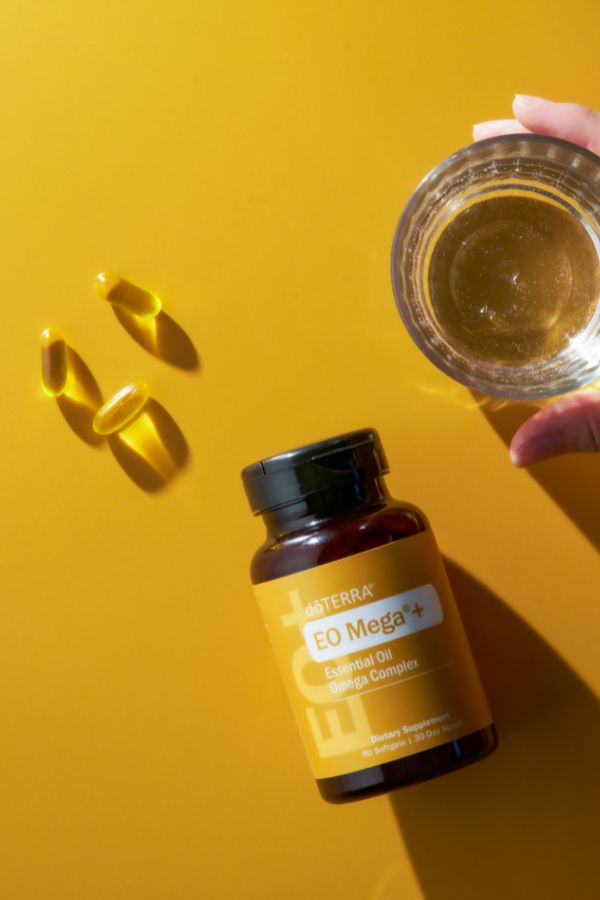 Bottle of Eterra EO Mega+ on a yellow background with capsules and a glass.